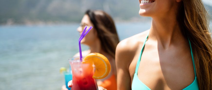 Beautiful young girls drinking cocktails during summer vacation on beach