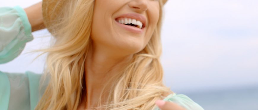 Close Up of Smiling Blond Woman Looking Elated and Happy Wearing Sun Hat near Ocean with Hair Blowing in Breeze
