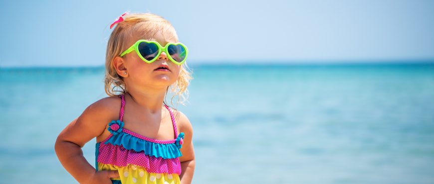 Cute little blond girl on the beach wearing sunglasses and stylish colorful swimsuit, child's fashion, summer vacation near the sea