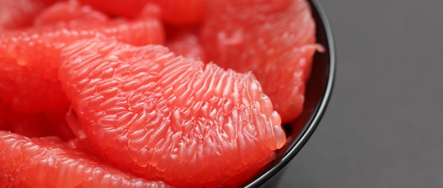 Red Grapefruit slices in a black bowl on black background. Close-up.