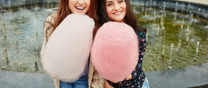Two cheerful sisters eating cotton candy at the park