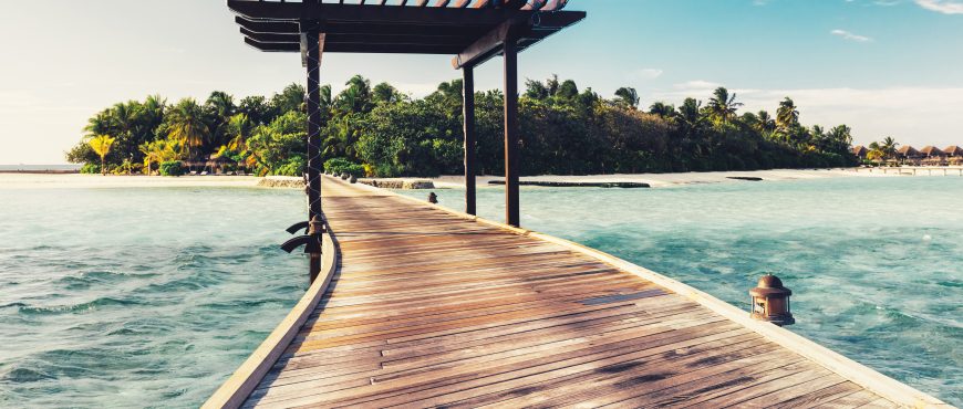 Wooden jetty with arch leading to a tropical island. Water landscape. Maldives destination